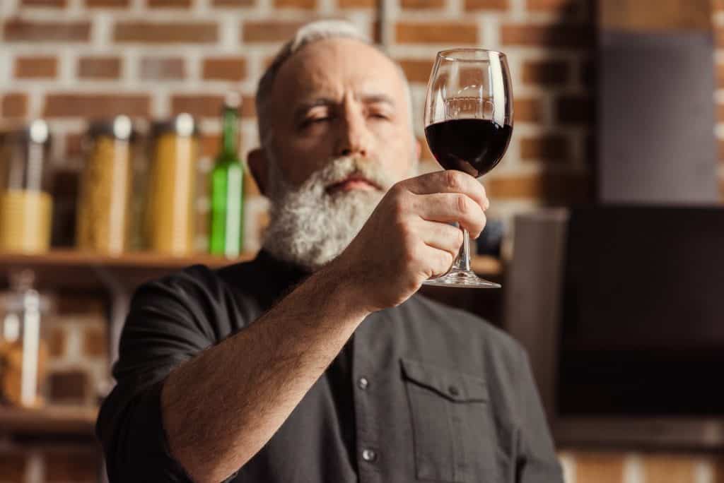 Bearded senior man looking at wine glass with red wine